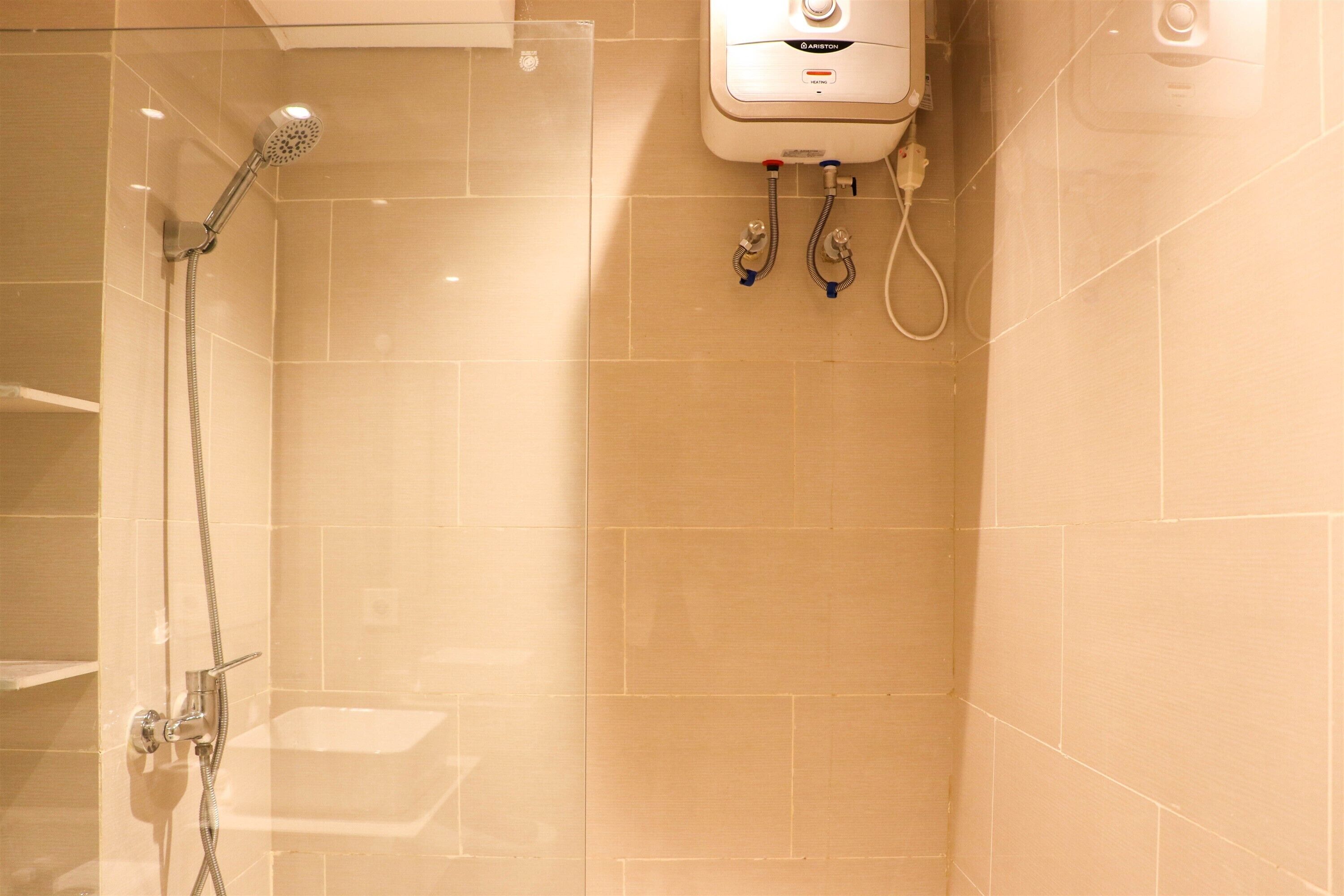 A shower area with a handheld showerhead, a wall-mounted control panel, and a toilet.
