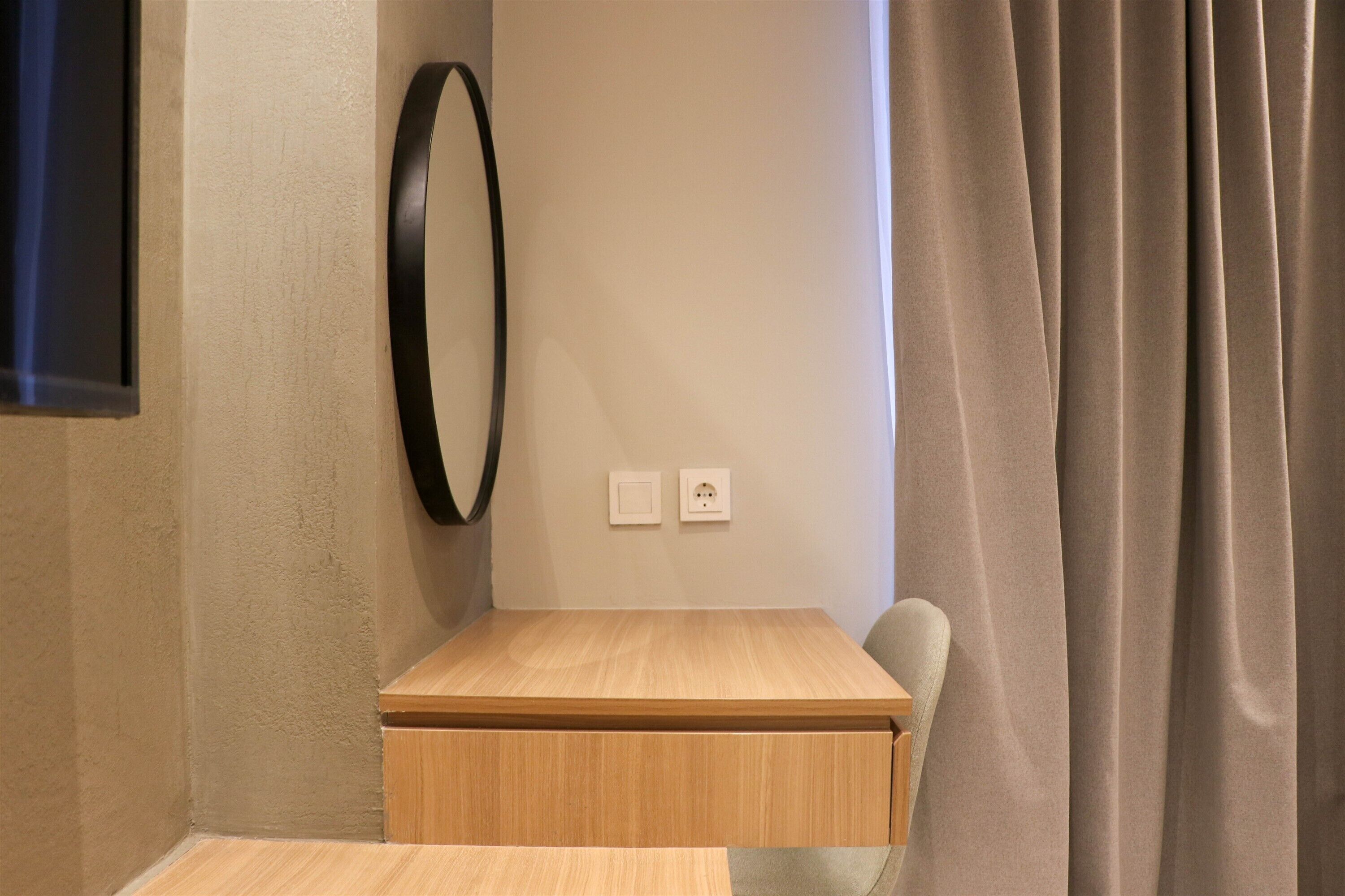 A small room with a wooden table, a chair, a wall-mounted mirror, and a curtain.