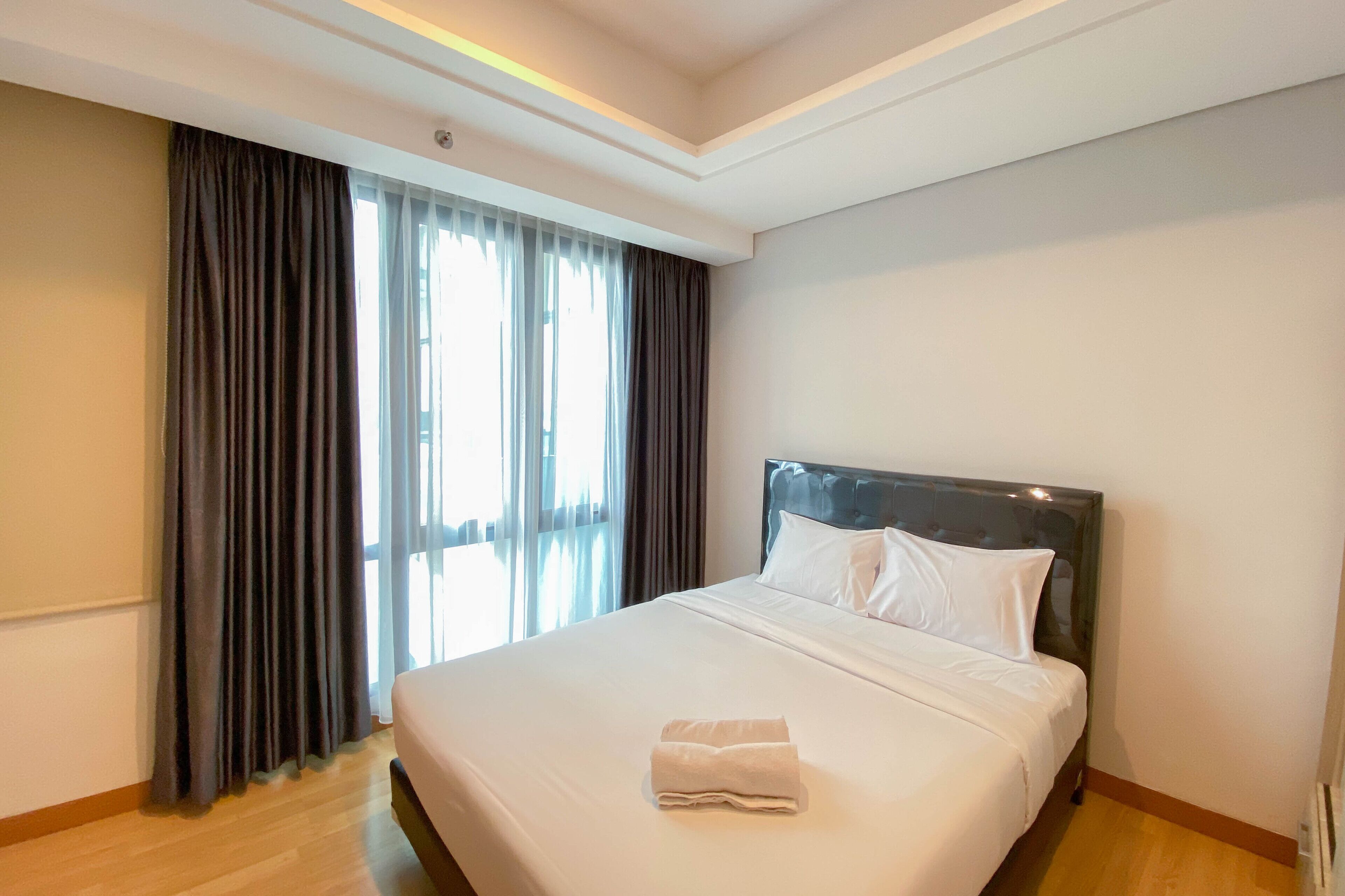 A hotel room with a large bed, a headboard, and a window with curtains.