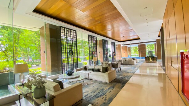 Un hall d’hôtel moderne avec une paroi en verre, des sièges confortables et une vue sur la verdure environnante.