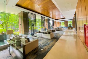 A modern hotel lobby with a glass partition, comfortable seating, and a view of greenery outside. - Stunning And Homey Studio Capitol Suites Apartment (Jakarta)