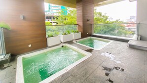 Un espace piscine intérieur moderne, doté de deux piscines rectangulaires, entouré d’un mur en bois et d’une rambarde en verre.