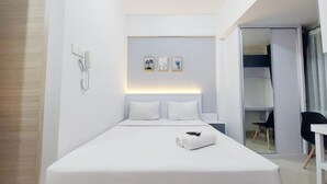 Una habitación de hotel moderna con una cama bien hecha, una mesita de noche y un pequeño escritorio. Hay tres cuadros enmarcados en la pared sobre la cama.