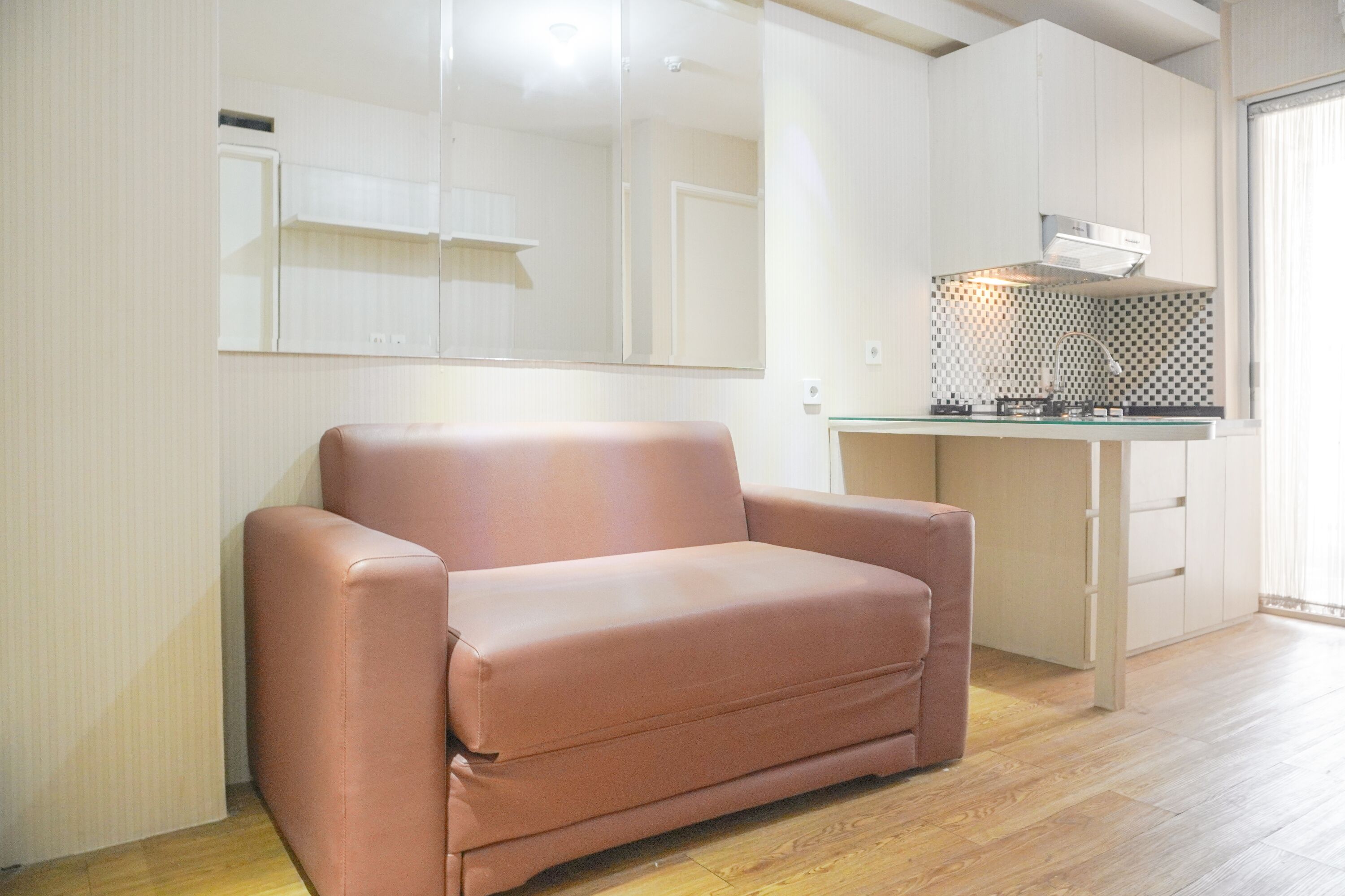 Uma sala de estar moderna com sofá, cozinha com fogão e um espelho grande na parede.