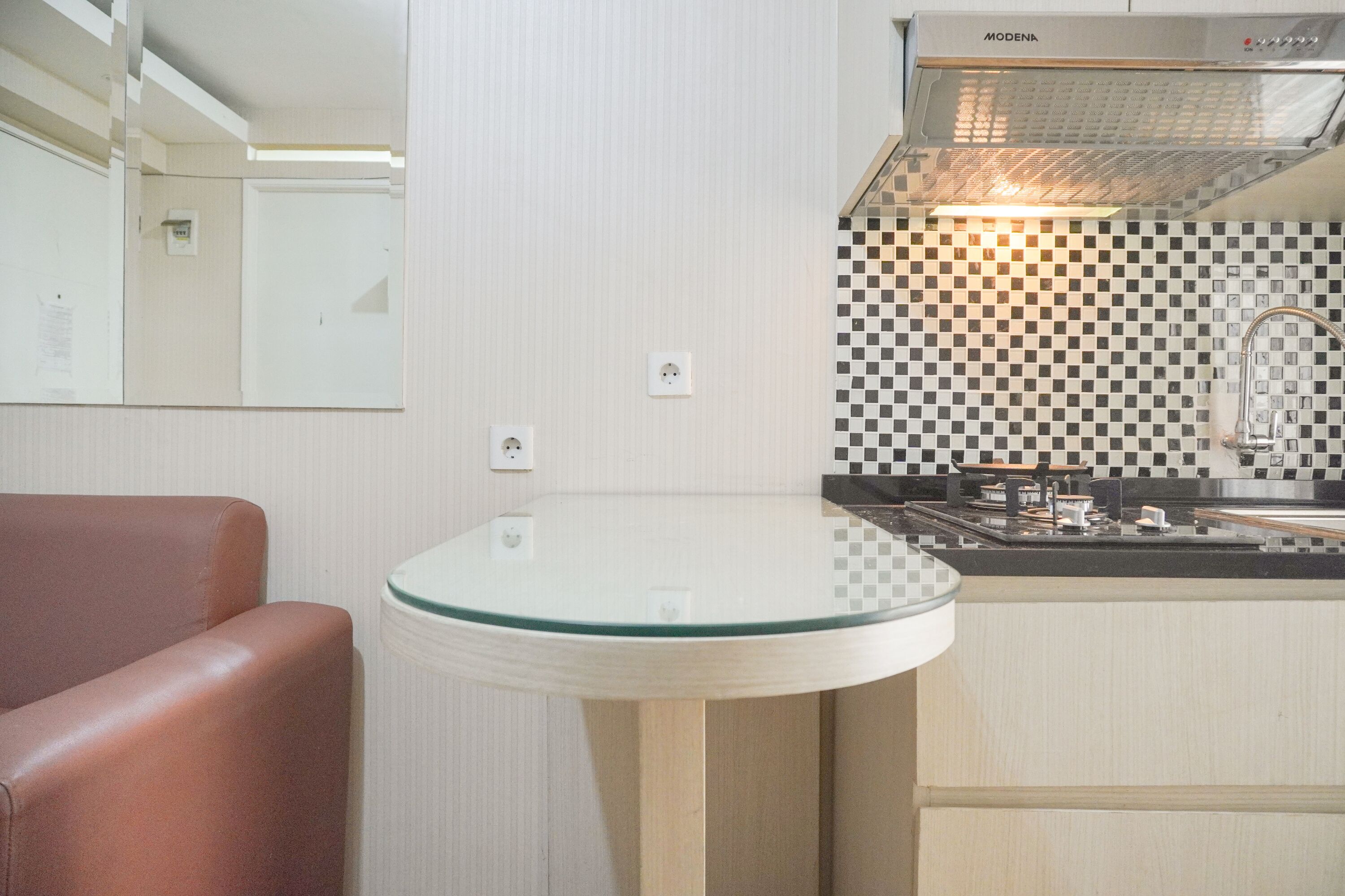 A compact kitchen with a glass-top table, a built-in stove, and a checkered backsplash.