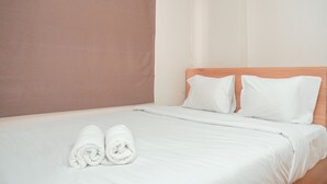 A neatly made bed with white linens and pillows, a wooden headboard, and a pair of rolled towels on the bed.