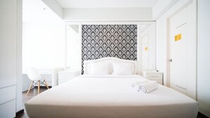 A modern hotel room with a neatly made bed, a white desk, and a chair.