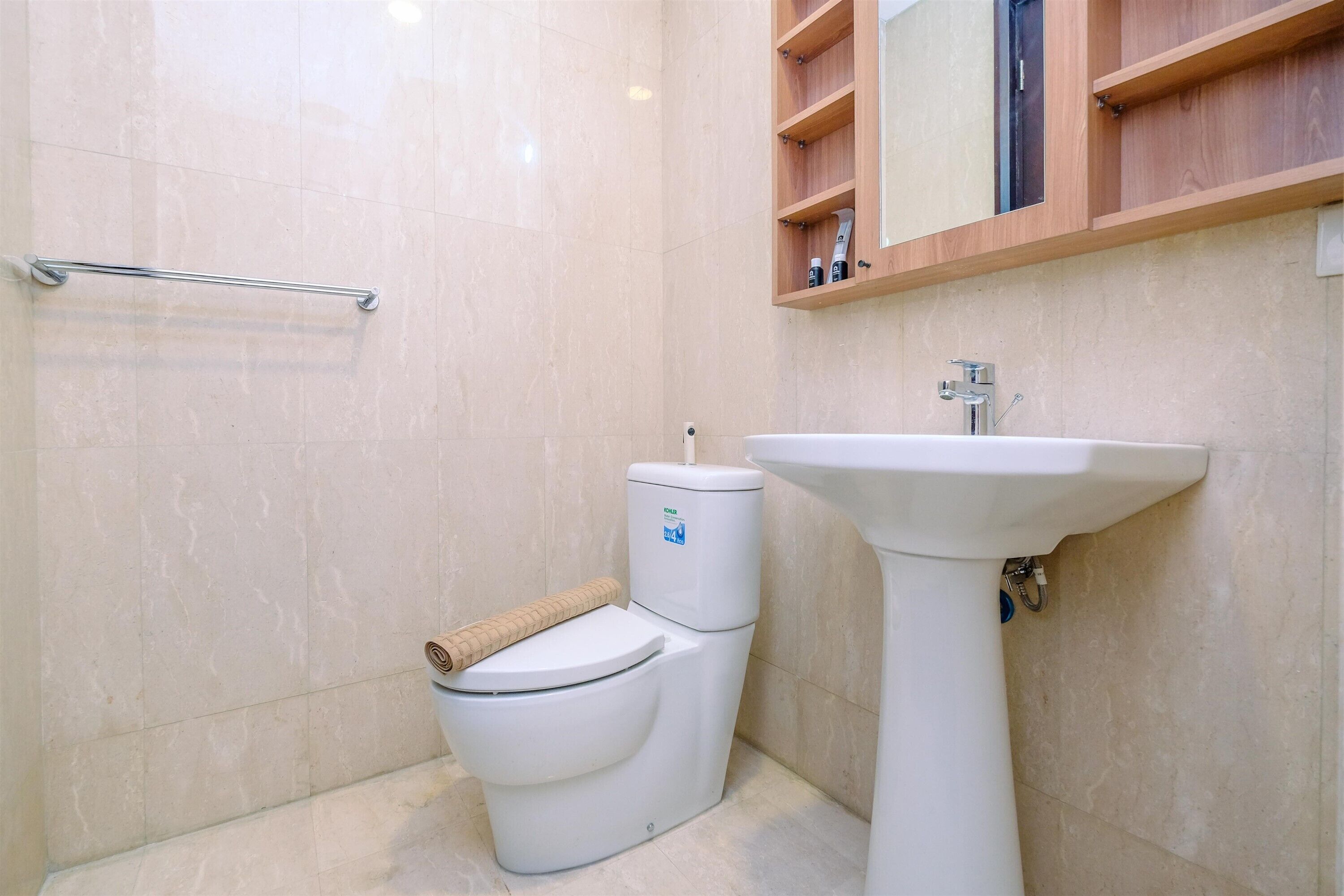 A bathroom with a toilet, sink, and wooden shelves above the mirror.