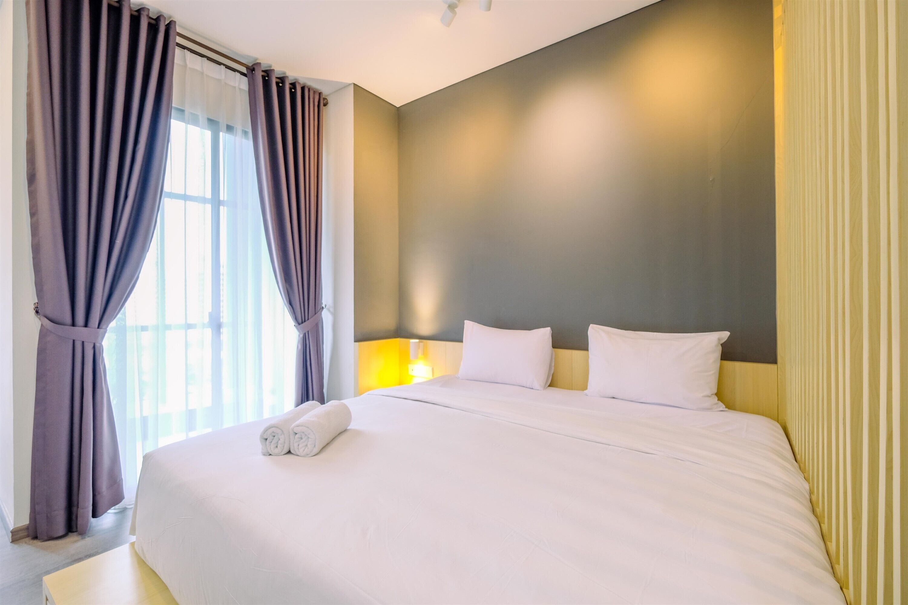 A hotel room with a large bed, a nightstand, a lamp, and curtains.