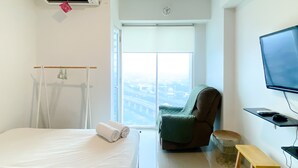 Una camera d'albergo con un letto, una sedia, un tavolino, una TV e una finestra con vista sulla città.