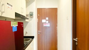 Un corridoio stretto con una porta in legno, un frigorifero rosso e un lavandino bianco.