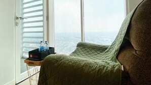 Una stanza con una grande finestra, un letto, un comodino con bottiglie d'acqua e vista sulla città.