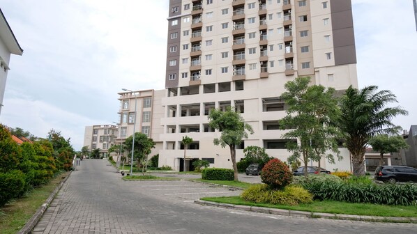 Un edificio residencial de varios pisos con balcones, una calle pavimentada y zonas verdes aledañas.
