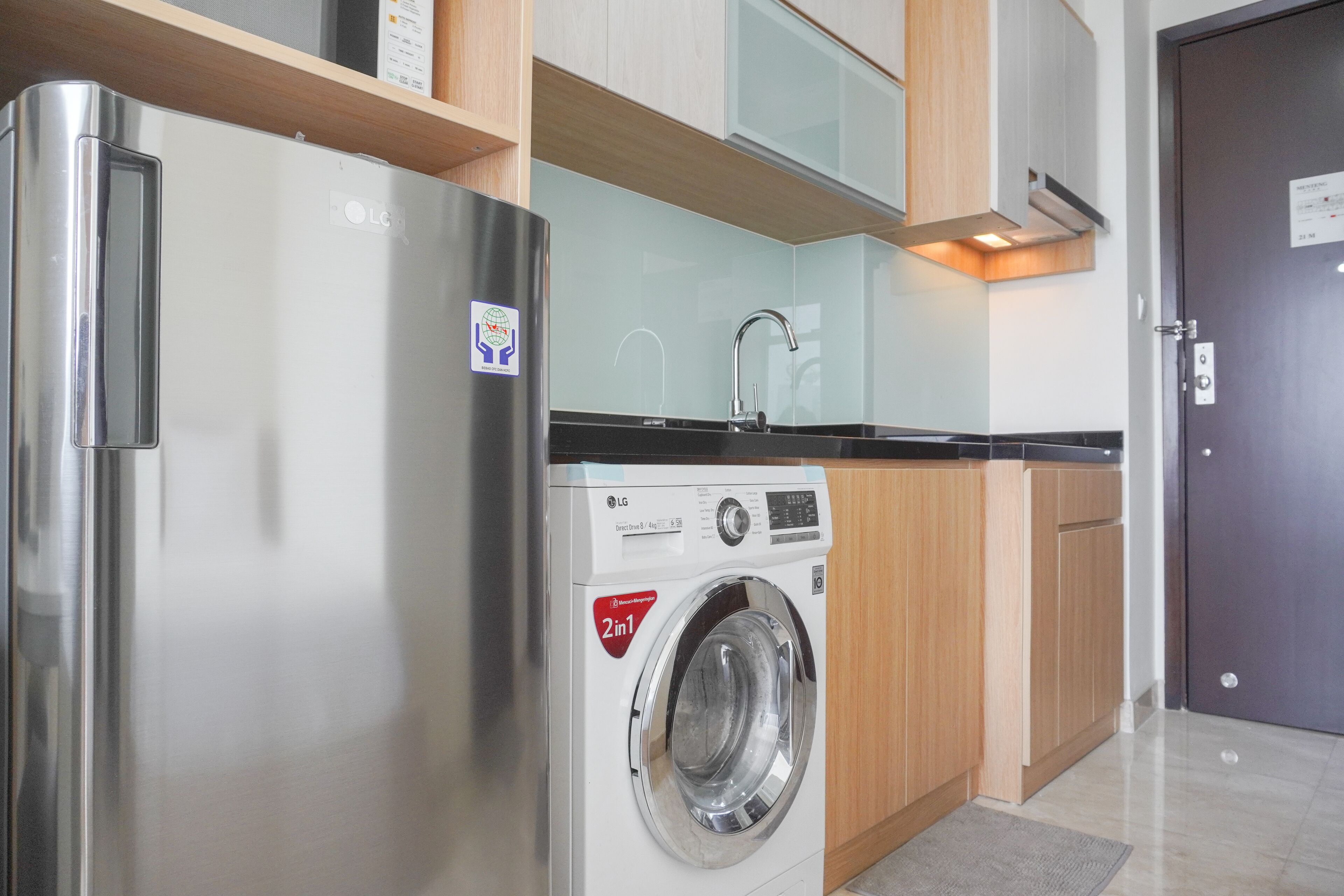 A compact kitchen with a stainless steel refrigerator, a washing machine, and wooden cabinets.