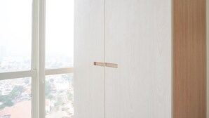 A view of a white wardrobe with a wooden panel in the center, next to a window with a view of buildings. - Comfort And Minimalist Studio Menteng Park Apartment (Jakarta)