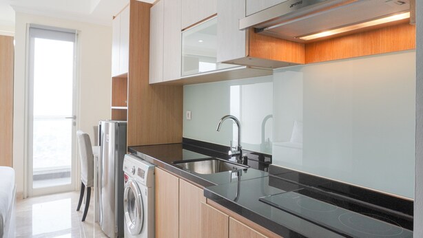 A modern kitchen with stainless steel appliances, a black countertop, and wooden cabinetry. - Comfort And Minimalist Studio Menteng Park Apartment (Jakarta)