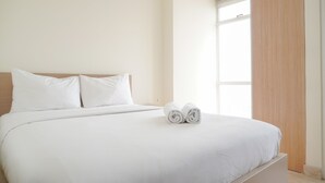 A neatly made bed with white linens and pillows, a pair of rolled towels on the bed, and a large window with a view of the outside. - Comfort And Minimalist Studio Menteng Park Apartment (Jakarta)