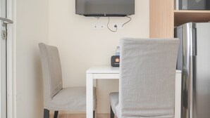 A small dining area with two chairs, a table, a TV mounted on the wall, and a microwave above the table. - Comfort And Minimalist Studio Menteng Park Apartment (Jakarta)