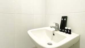Un lavamanos blanco con un solo grifo en un rincón de una habitación con paredes de azulejos blancos.