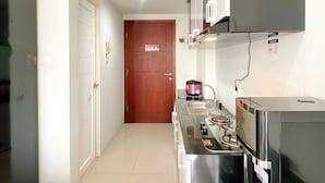 Cocina compacta con estufa, microondas y refrigerador pequeño. Una puerta de madera conduce a otra habitación.