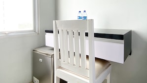 Un escritorio pequeño y blanco con dos botellas de agua encima, una silla blanca y un mueble bajo también blanco.