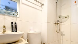 Casa de banho com lavatório branco, sanita e chuveiro. Existem duas embalagens de produtos de higiene no balcão do lavatório.