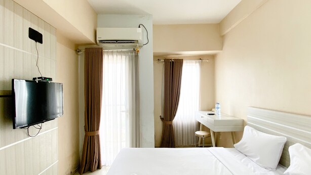 Quarto de hotel com uma cama, televisão na parede, secretária pequena com cadeira e unidade de ar condicionado.