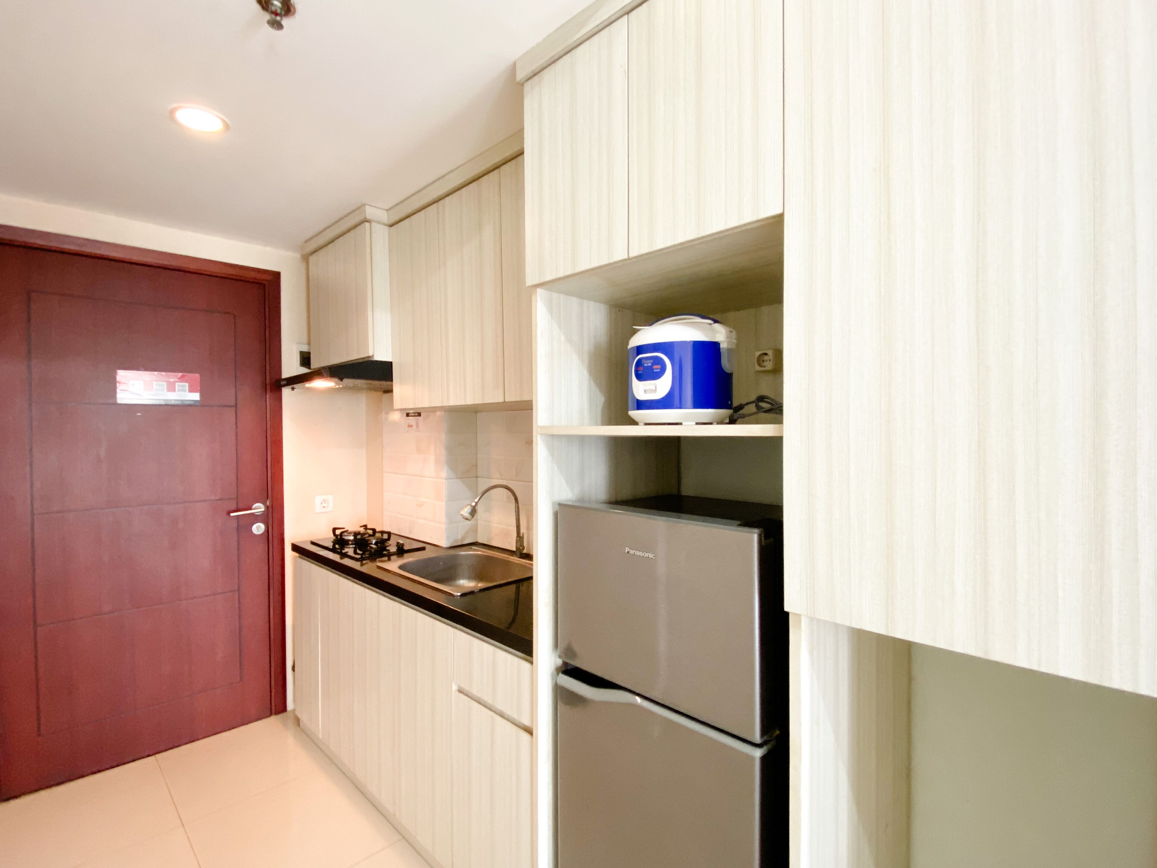 A kitchen with white cabinets, a red door, a gas stove, a sink, and a refrigerator.