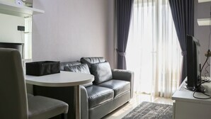 A modern living room with a grey leather sofa, a small round table, and a TV on a stand. - Minimalist And Warm 1Br Signature Park Grande Apartment (Jakarta)