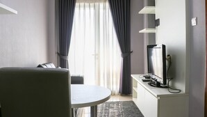 A room with a dining table, a TV on a stand, and a window with curtains. - Minimalist And Warm 1Br Signature Park Grande Apartment (Jakarta)