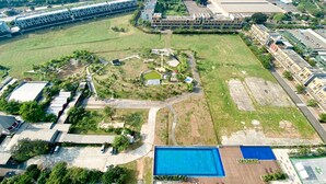 An aerial view of a large, undeveloped plot with a swimming pool, surrounded by buildings and roads. - Spacious And Homey 1Br Vasanta Innopark Apartment (Cikarang)