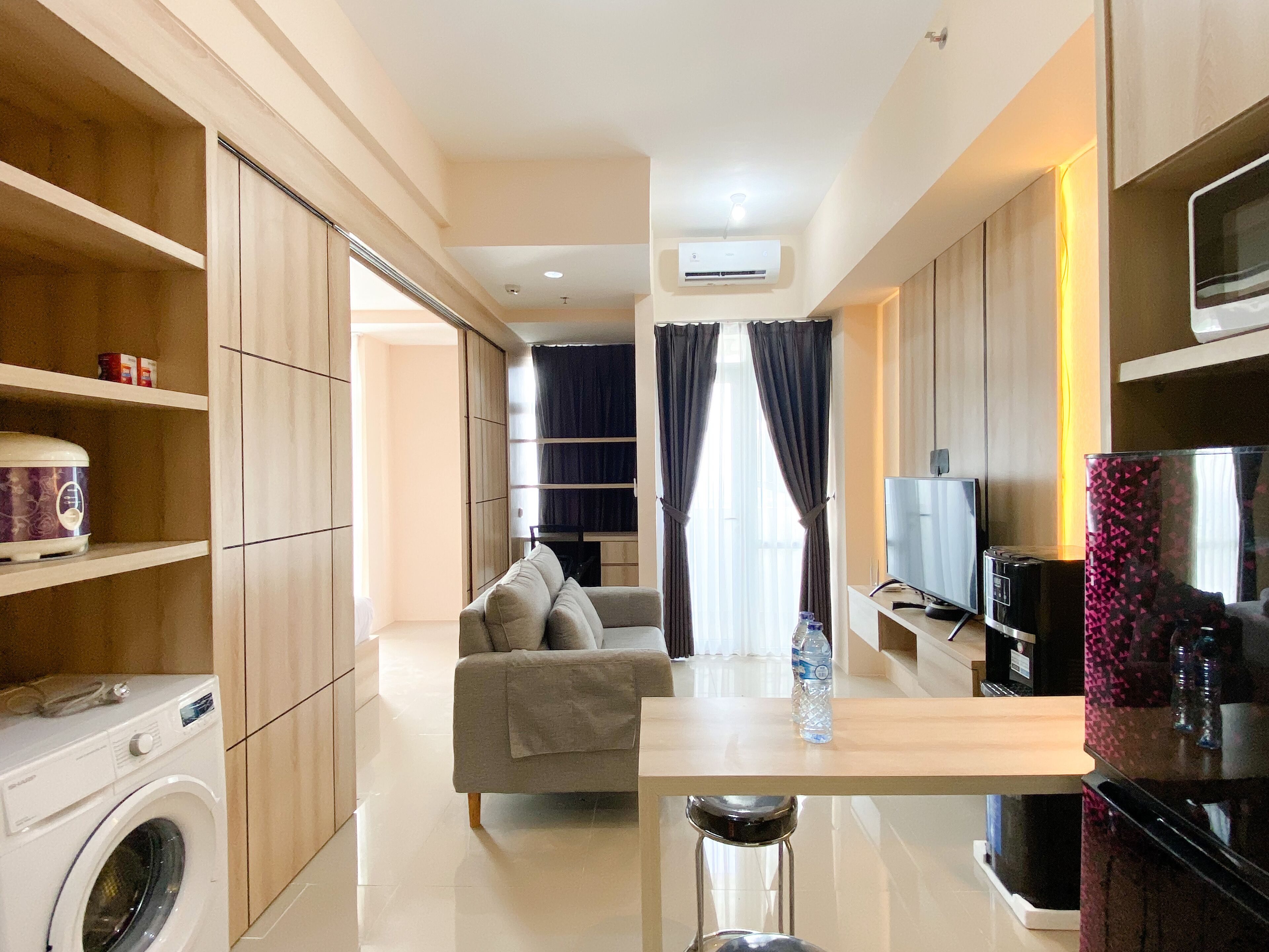 A modern kitchen with a washing machine, a dining area with a table and chairs, a sofa, and a TV.