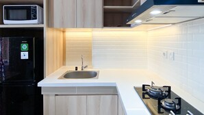 A modern kitchen with a built-in microwave, a black refrigerator, a sink, and a gas stove. - Spacious And Homey 1Br Vasanta Innopark Apartment (Cikarang)