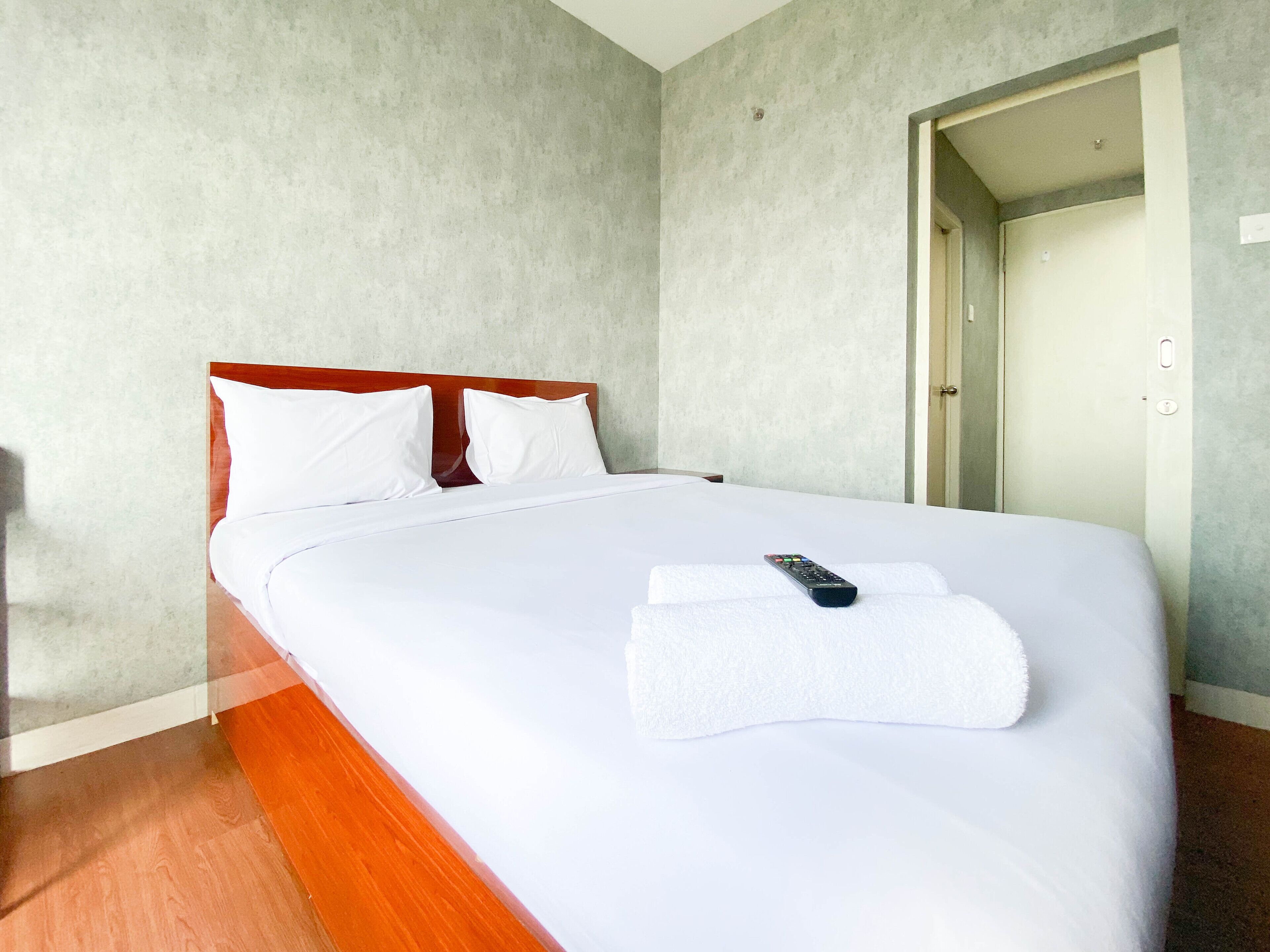 A neatly made bed with white linens and a remote control on the bed.