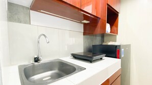 A kitchen with a stainless steel sink, a built-in microwave, and wooden cabinets. - Homey And Good Choice Studio At Amartha View Apartment (Semarang)