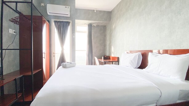 A hotel room with a large bed, a desk, a chair, and a wardrobe. - Homey And Good Choice Studio At Amartha View Apartment (Semarang)