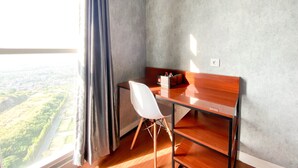 A modern room with a wooden desk, a white chair, and a view of greenery through a window. - Homey And Good Choice Studio At Amartha View Apartment (Semarang)