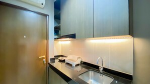 A modern kitchen with a black countertop, stainless steel sink, and a built-in oven. - Cozy And Minimalist Studio Room Ciputra International Apartment (Jakarta)