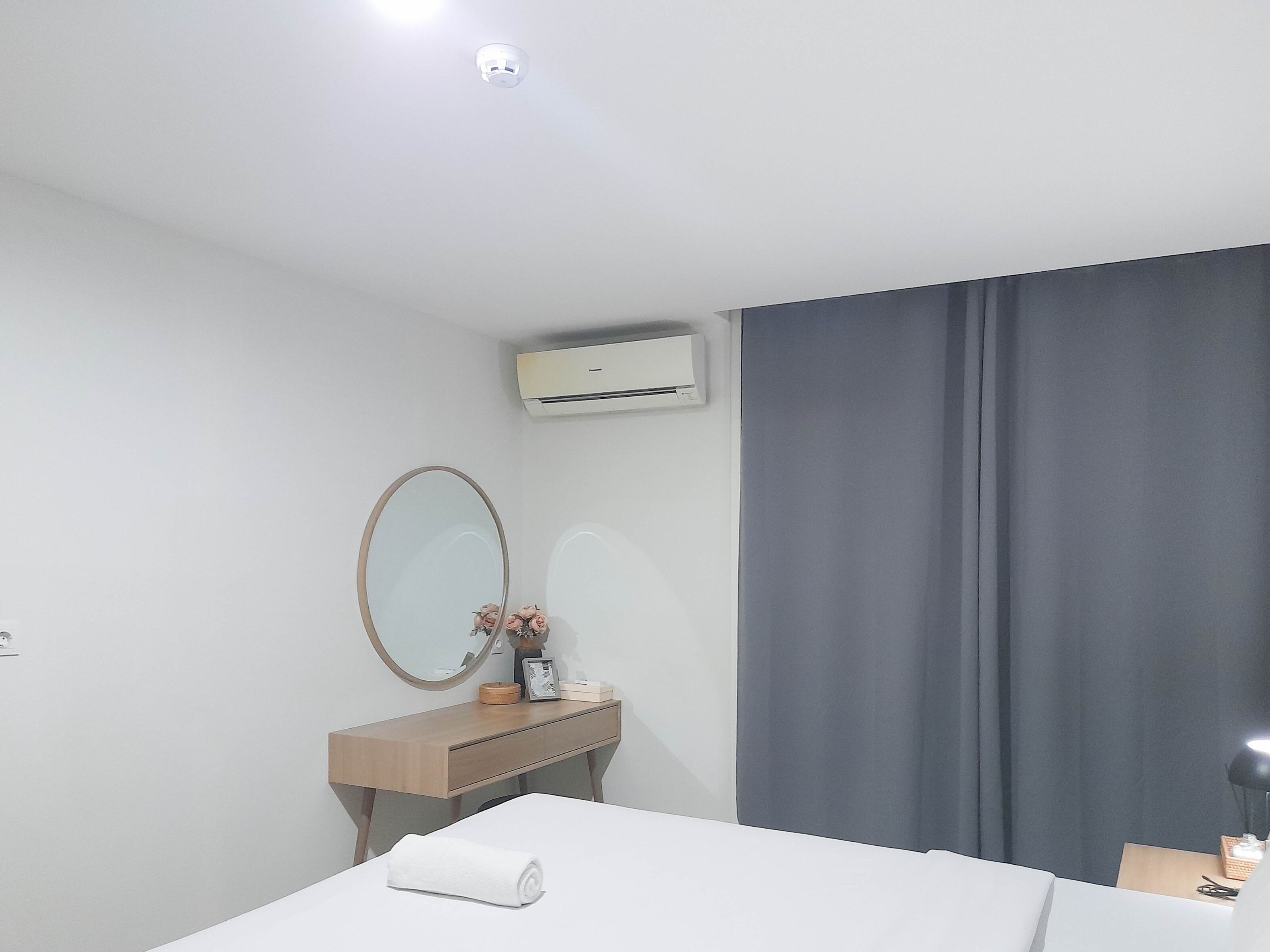 Quarto de hotel com cama, cómoda de madeira, espelho, ar condicionado e uma janela grande com cortinas.