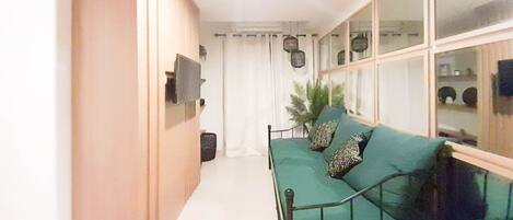 A compact living space with a green sofa, a wooden cabinet, and a large window with a view.