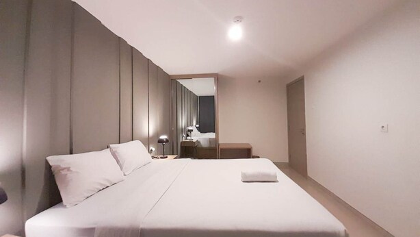 Moderni hotellihuone, jossa on suuri sänky, yöpöytä, lamppu ja peili.