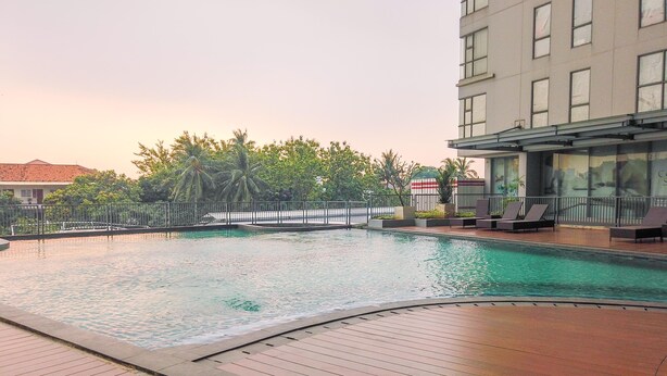 Ein Pool mit Holzterrasse, umgeben von einem Zaun und Palmen.