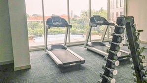 Ein Fitnessstudio mit Laufbändern und Hanteln, großen Fenstern und Blick auf Gebäude und Bäume.