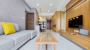 A modern living room with a grey sofa, a wooden coffee table, and a TV mounted on a wooden wall. - Comfort And Spacious 3Br At Sky House Bsd Apartment (Pagedangan)
