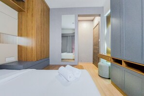 A hotel room with a bed, a wooden wardrobe, a mirror, and a small seating area. - Comfort And Spacious 3Br At Sky House Bsd Apartment (Pagedangan)