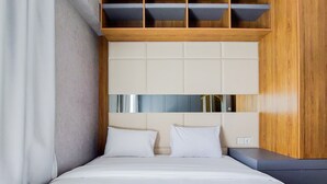A modern bedroom with a bed, two pillows, a wooden headboard, and a built-in bench. - Comfort And Spacious 3Br At Sky House Bsd Apartment (Pagedangan)