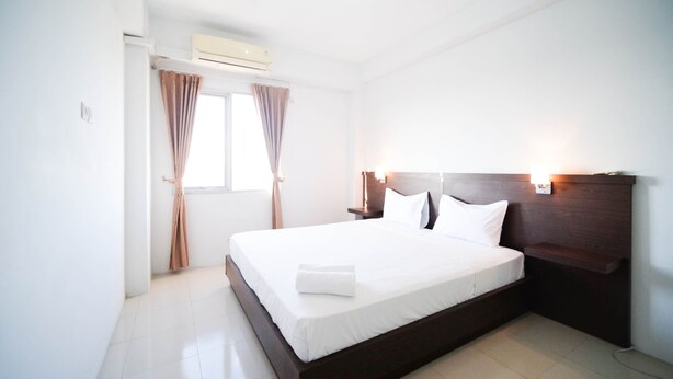 A hotel room with a single bed, a nightstand, an air conditioning unit, and a window with curtains. - Simple 2Br With Extra Bed At Menara Rungkut Apartment (Surabaya)
