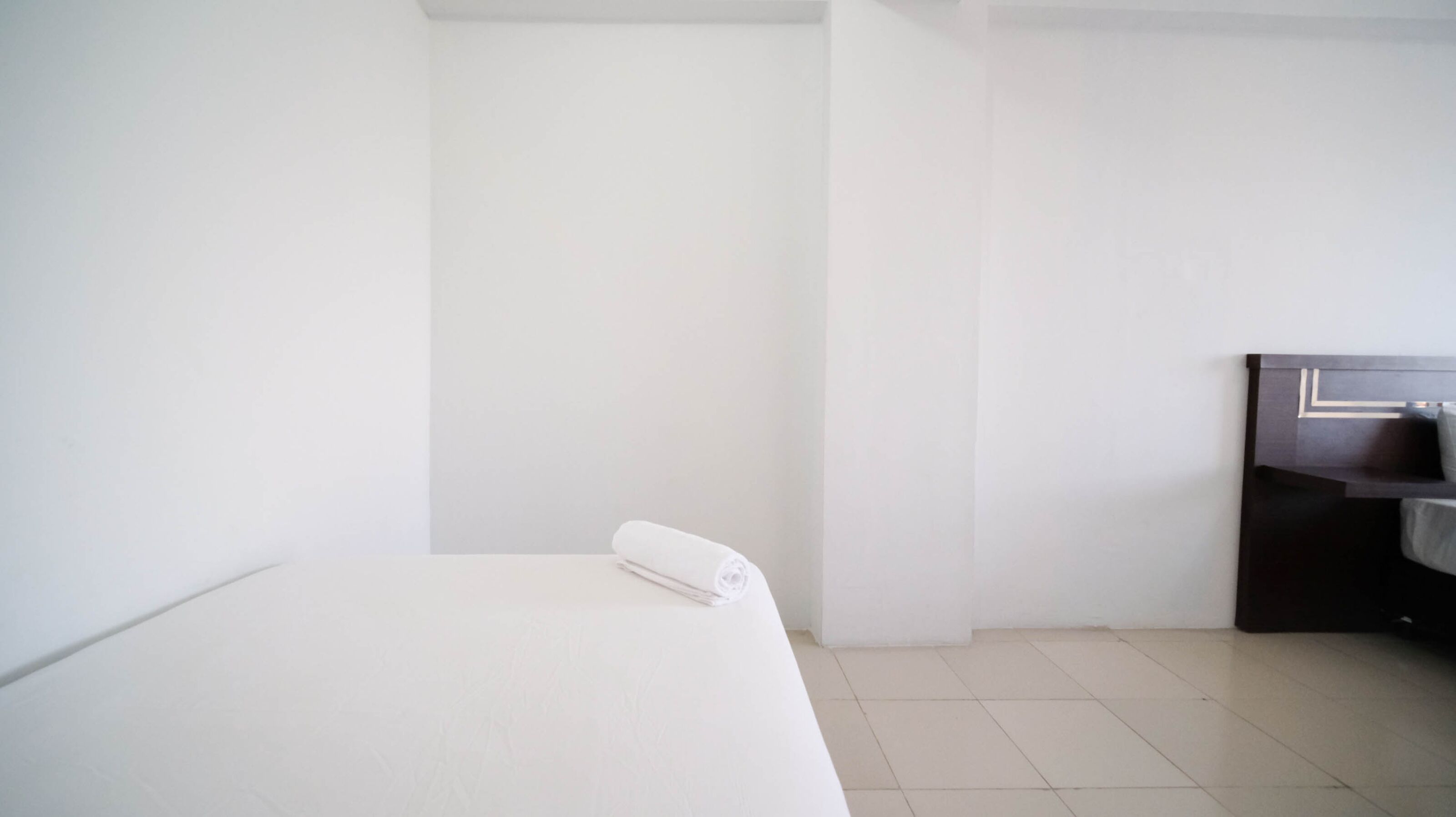 A hotel room with a bed, a small desk, and a white towel on the bed.
