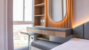 Quarto moderno com uma cama grande, mesa de cabeceira, espelho e janela com vista para prédios.