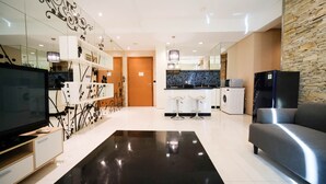 A modern living room with a flat-screen TV, a sofa, a black rug, and a kitchen area with a washing machine.